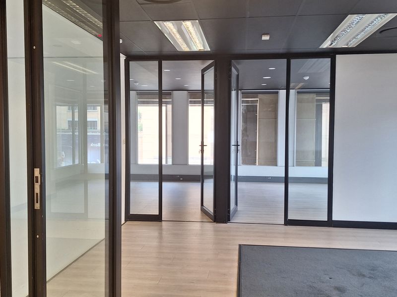 Modern open-plan office space featuring glass partitions, recessed lighting, and a combination of laminate and carpet flooring, offering a bright and professional work environment.