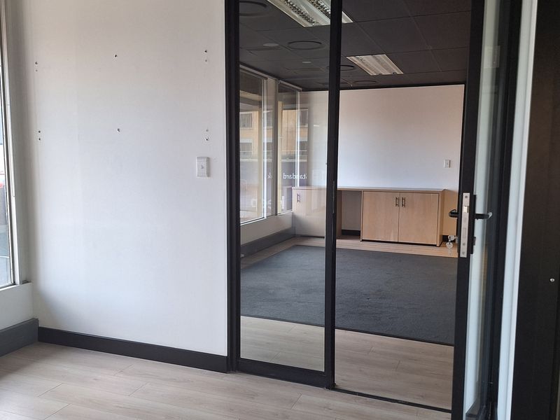 A bright, modern office space featuring a glass partition, light wood-look laminate flooring, and built-in cabinetry, offering a clean and professional work environment.