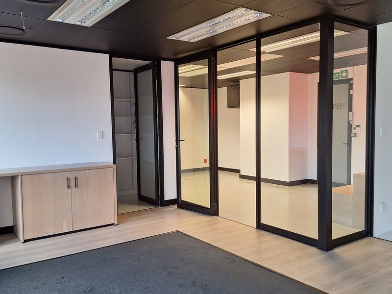 Modern office space featuring glass partitions, a sleek black suspended ceiling with recessed lighting, and light wood-tone built-in cabinetry.