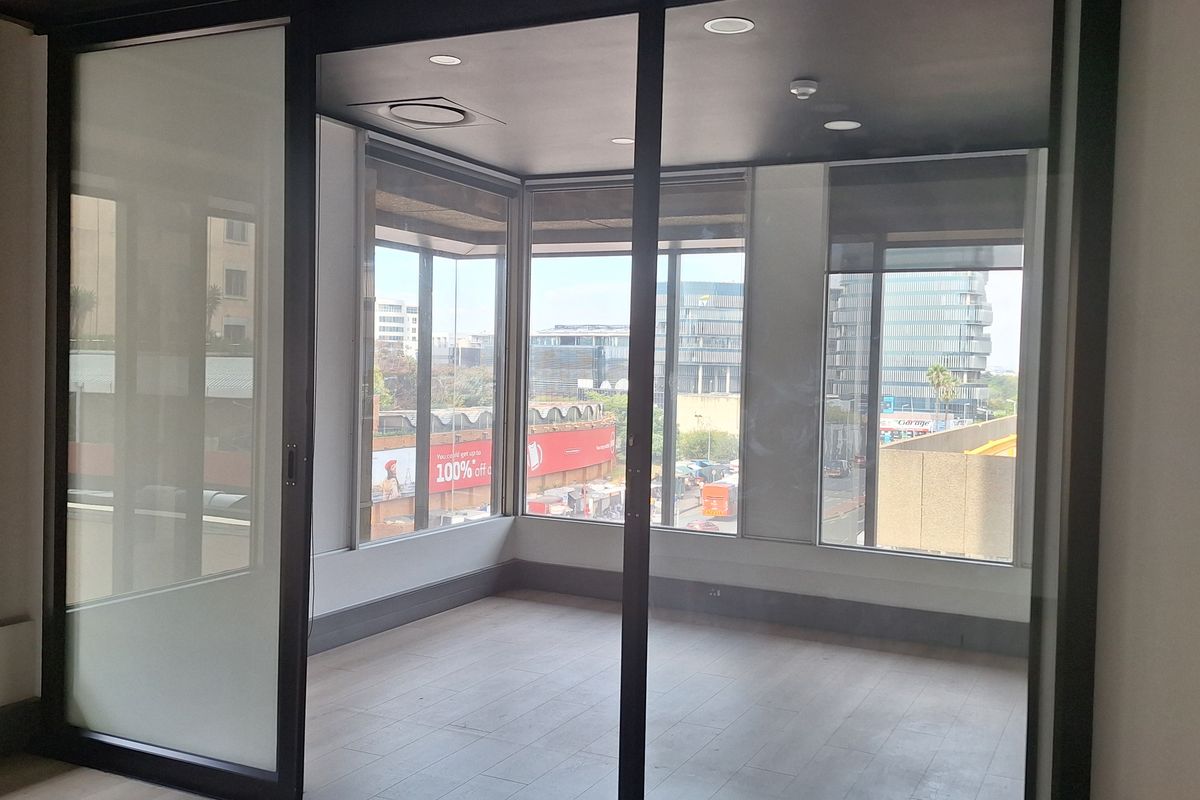 A modern, empty office space featuring large windows, laminate flooring, and a sleek sliding glass partition, offering a bright and professional work environment.