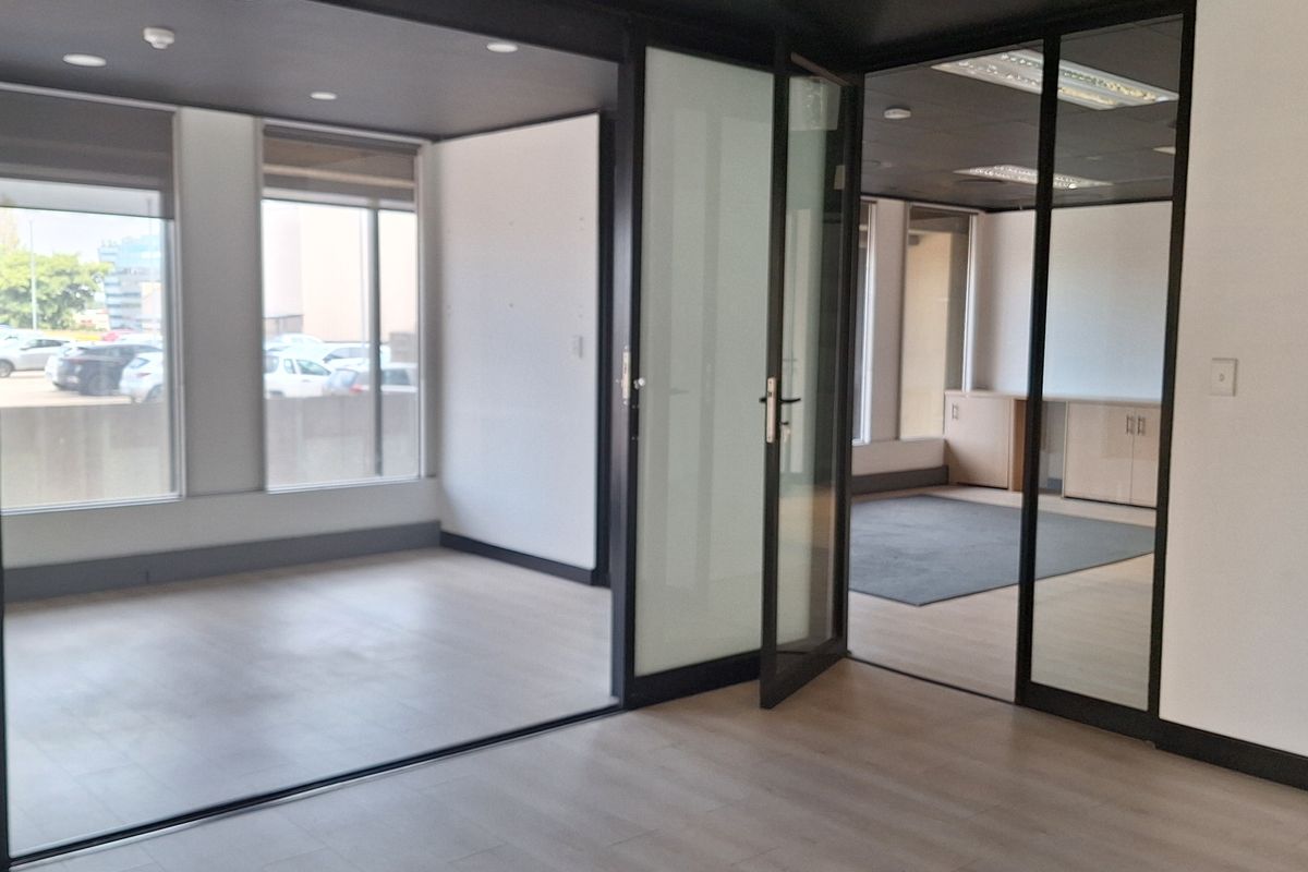 Modern office space featuring laminate flooring, recessed lighting, and sleek black-framed glass partitions creating a bright, professional, and open-plan working environment.