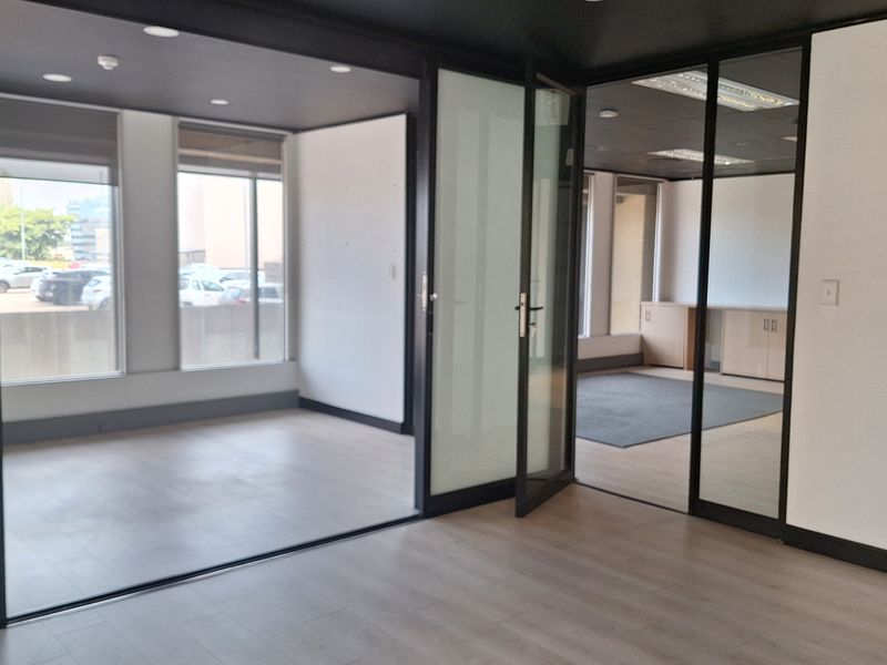 Modern office space featuring laminate flooring, recessed lighting, and sleek black-framed glass partitions creating a bright, professional, and open-plan working environment.