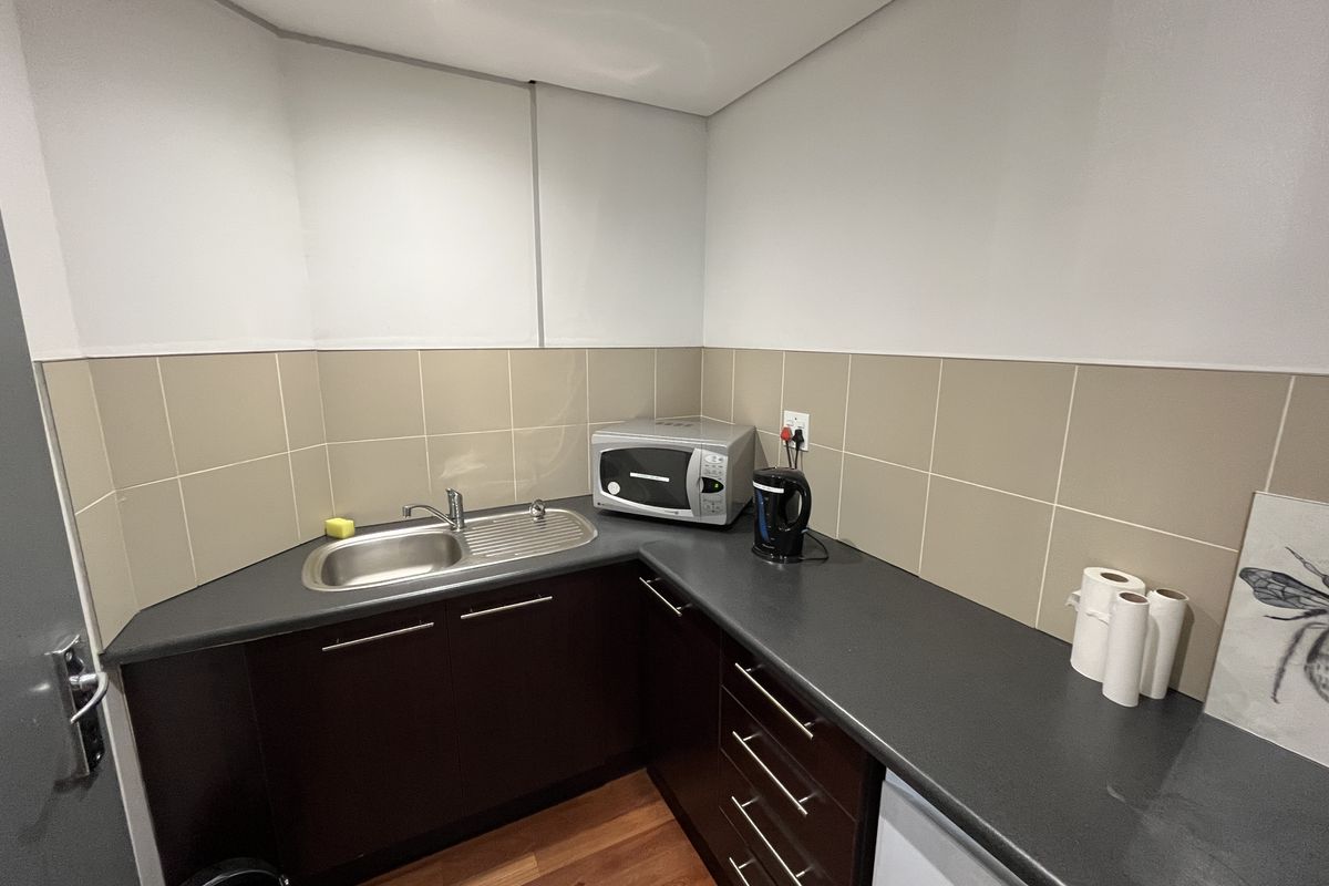 A compact office kitchenette featuring dark cabinetry, a stainless steel sink, and neutral tiled splashbacks.
