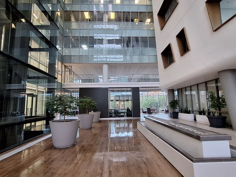 Spacious modern office atrium featuring a glass curtain wall, polished wood-look flooring, and a built-in water feature in a bright, professional environment.