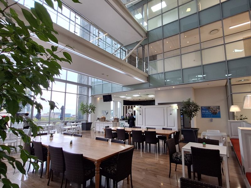 Spacious open-plan office atrium featuring high ceilings, extensive glass curtain walls, and modern hardwood flooring in a bright, multi-level commercial environment.
