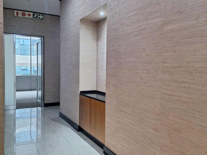 A modern office hallway featuring wood-paneled walls, polished tile flooring, and a built-in service cabinet with recessed lighting.