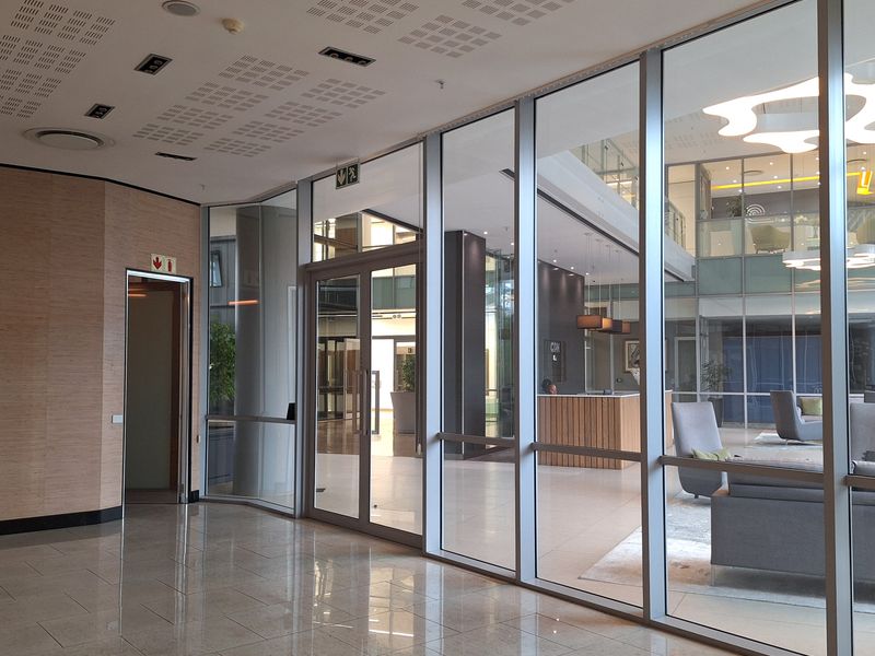 Modern office interior featuring extensive glass partitioning, polished tile flooring, and professional recessed ceiling lighting in a bright, open-plan corporate environment.
