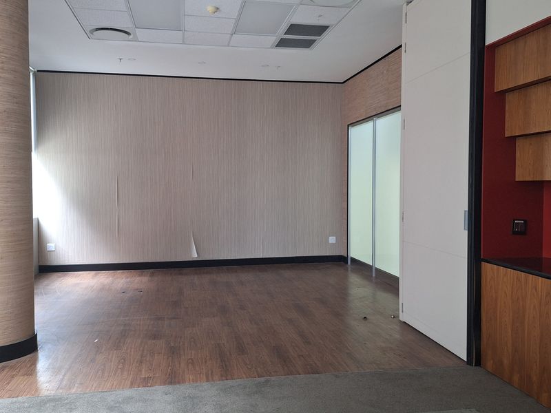 An empty office space featuring wood laminate flooring, a suspended ceiling with recessed lighting, and built-in cabinetry with a sliding partition door.