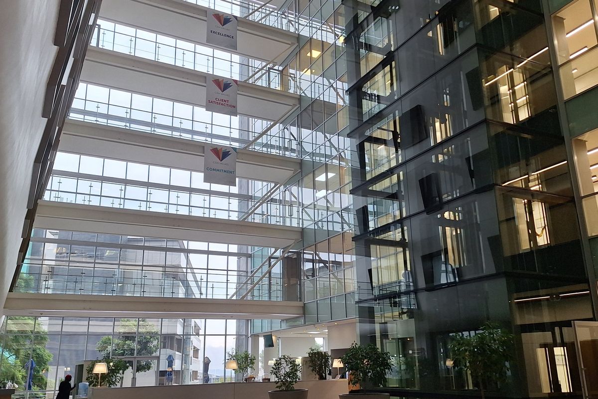 A modern, multi-story office atrium featuring a glass curtain wall, a prominent glass elevator shaft, and a spacious, well-maintained reception area.