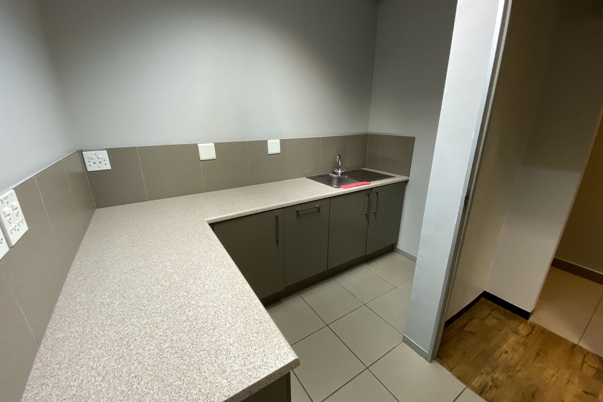 A functional office kitchenette featuring modern cabinetry, a laminate countertop, a stainless steel sink, and tiled splashbacks.