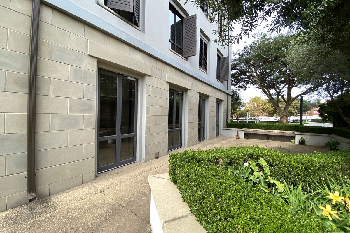 A well-maintained exterior rear view of the office building featuring stone-clad facade, dark-framed glass doors, and a landscaped patio area with built-in seating.