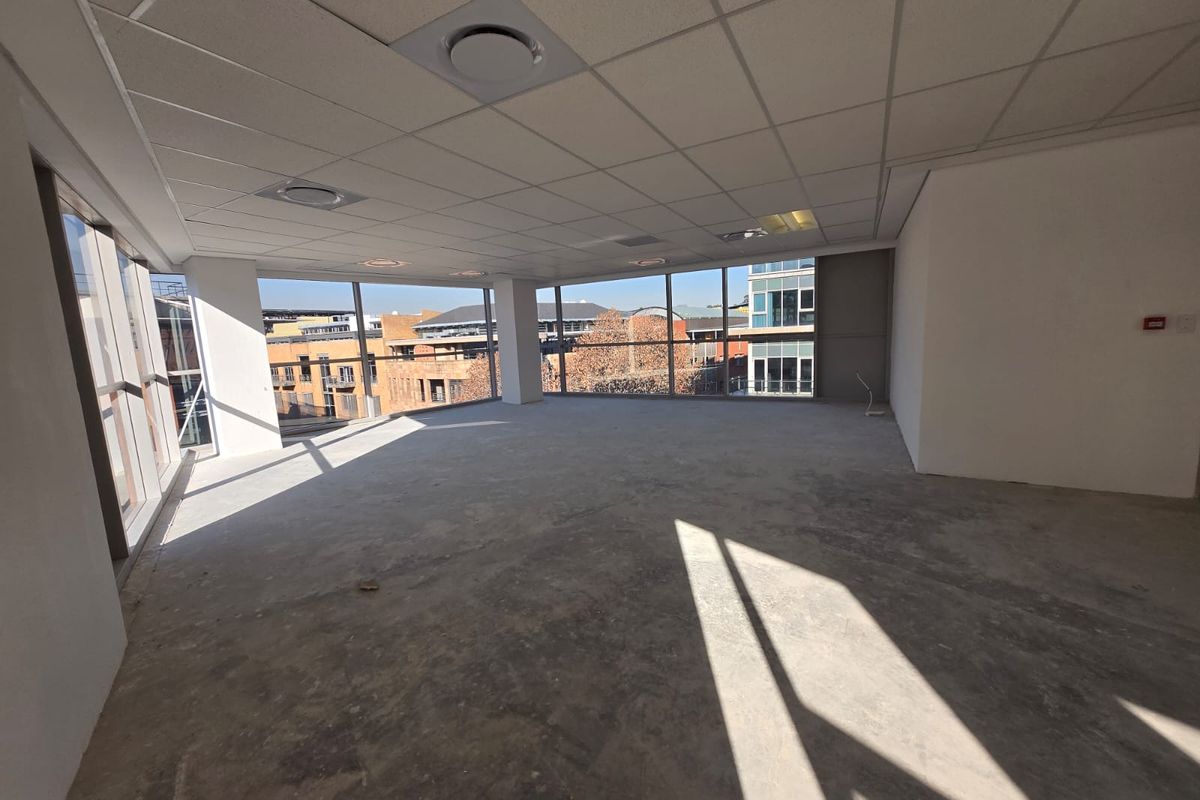 A bright, open-plan office space featuring floor-to-ceiling windows with urban views, a suspended ceiling, and unfinished concrete flooring ready for custom fit-out.