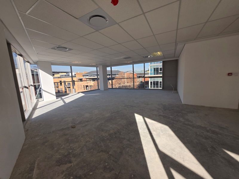 A bright, open-plan office space featuring floor-to-ceiling windows with urban views, a suspended ceiling, and unfinished concrete flooring ready for custom fit-out.