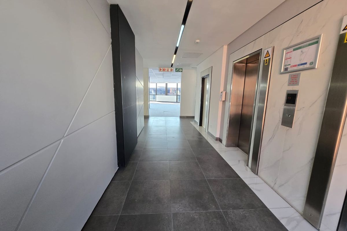 Modern office building hallway featuring sleek marble-effect wall cladding, stainless steel elevator doors, and contemporary recessed linear lighting with dark tiled flooring.