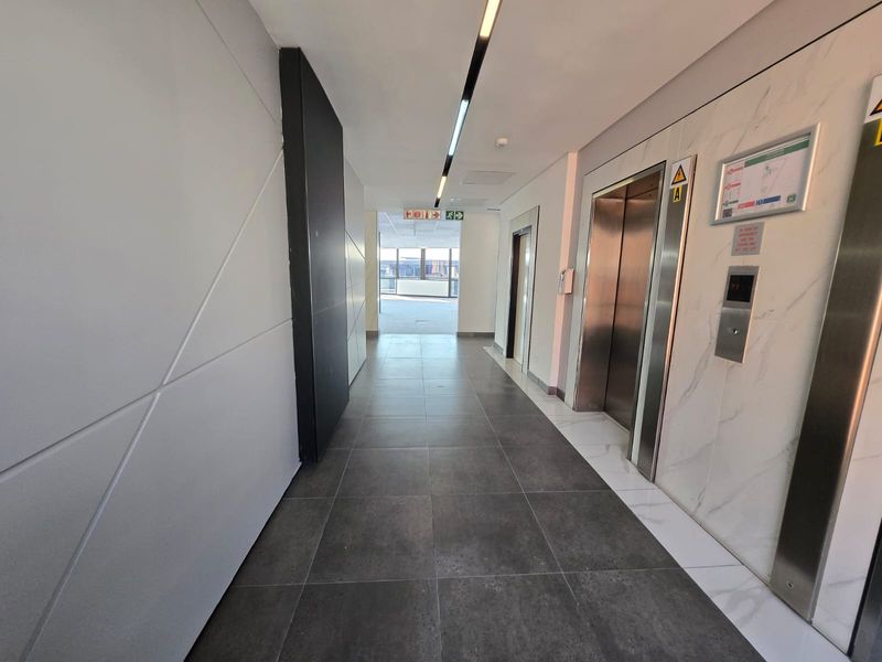Modern office building hallway featuring sleek marble-effect wall cladding, stainless steel elevator doors, and contemporary recessed linear lighting with dark tiled flooring.
