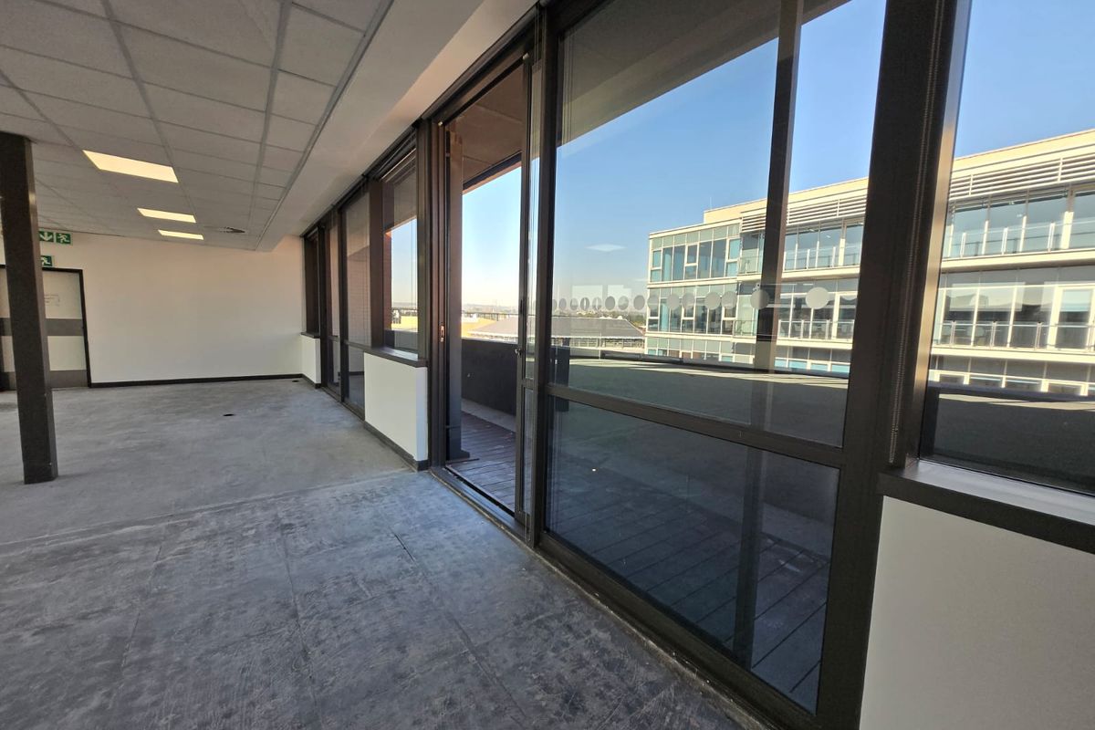 A bright, vacant office space featuring a suspended ceiling, recessed lighting, and large sliding glass doors leading to an outdoor balcony area.