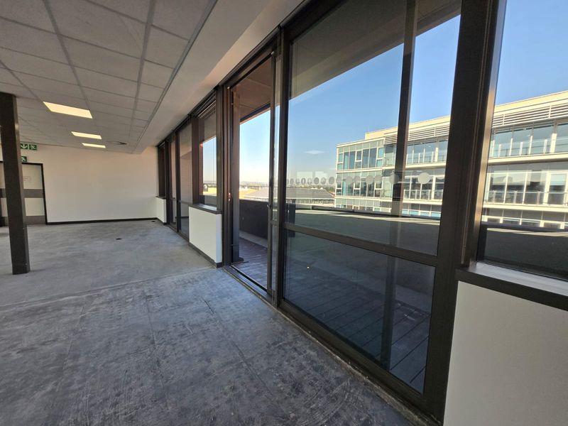 A bright, vacant office space featuring a suspended ceiling, recessed lighting, and large sliding glass doors leading to an outdoor balcony area.