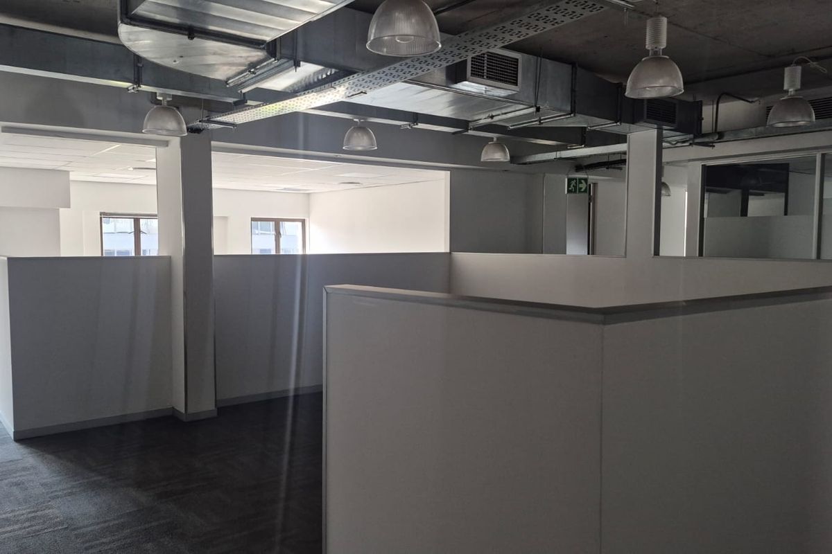 Open-plan office space featuring exposed industrial ceilings, modern partition walls, carpeted flooring, and integrated cable management systems.