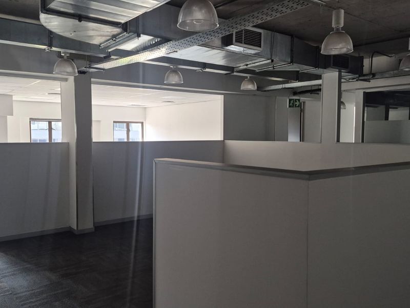 Open-plan office space featuring exposed industrial ceilings, modern partition walls, carpeted flooring, and integrated cable management systems.