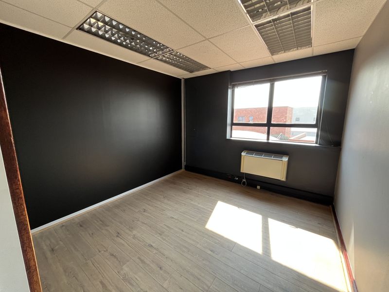 A vacant office space featuring laminate flooring, a suspended ceiling with recessed lighting, and a wall-mounted HVAC unit.