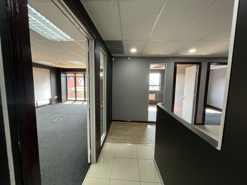 A modern office hallway featuring a mix of tiled, laminate, and carpeted flooring with access to multiple connected office spaces.