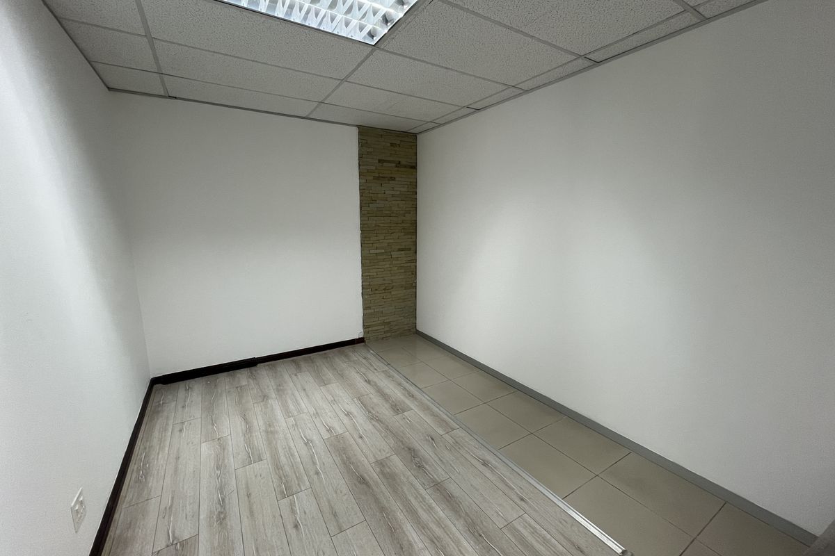 A vacant office space featuring a mix of laminate and tiled flooring, a stone accent wall, and a suspended ceiling with recessed lighting.