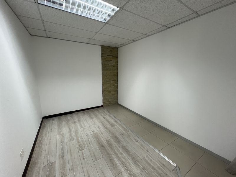 A vacant office space featuring a mix of laminate and tiled flooring, a stone accent wall, and a suspended ceiling with recessed lighting.