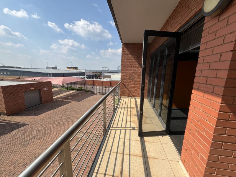 A spacious balcony with brick exterior, metal railings, and bi-fold glass doors providing access to the office interior.