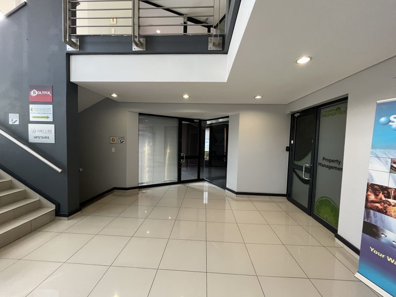 Modern office building entrance lobby featuring tiled flooring, a staircase with stainless steel railings, and glass-paneled office access doors.