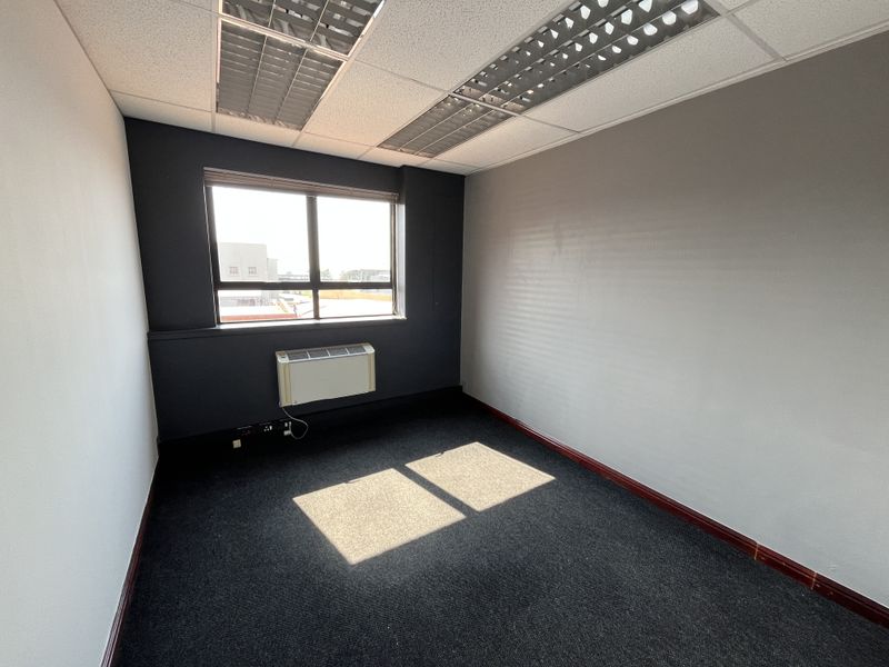 A vacant office space featuring dark carpeting, a suspended ceiling with recessed lighting, and a wall-mounted air conditioning unit.