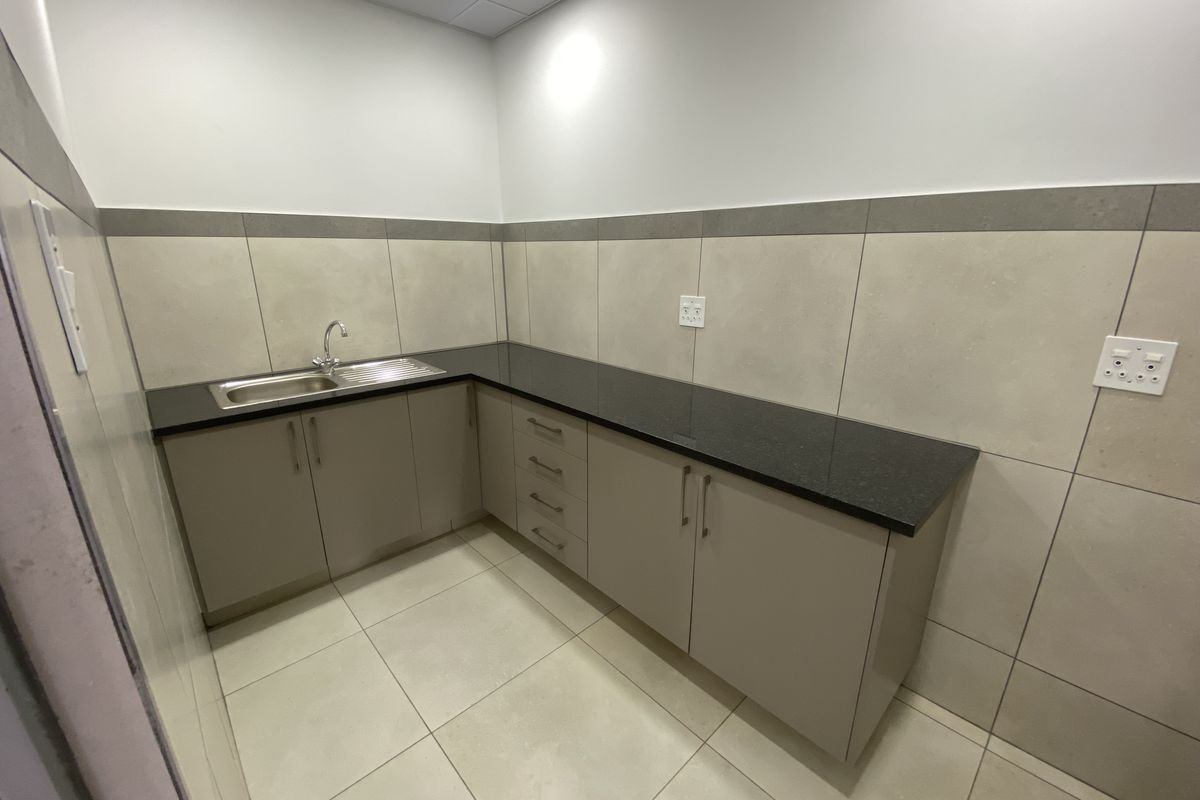 A clean and functional kitchenette area featuring modern cabinetry, a dark stone countertop, and a stainless steel sink with tiled splashbacks.