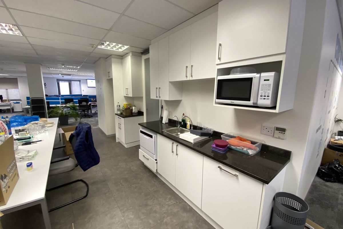 A functional office kitchenette featuring white cabinetry, dark stone countertops, a stainless steel sink, and a built-in microwave.