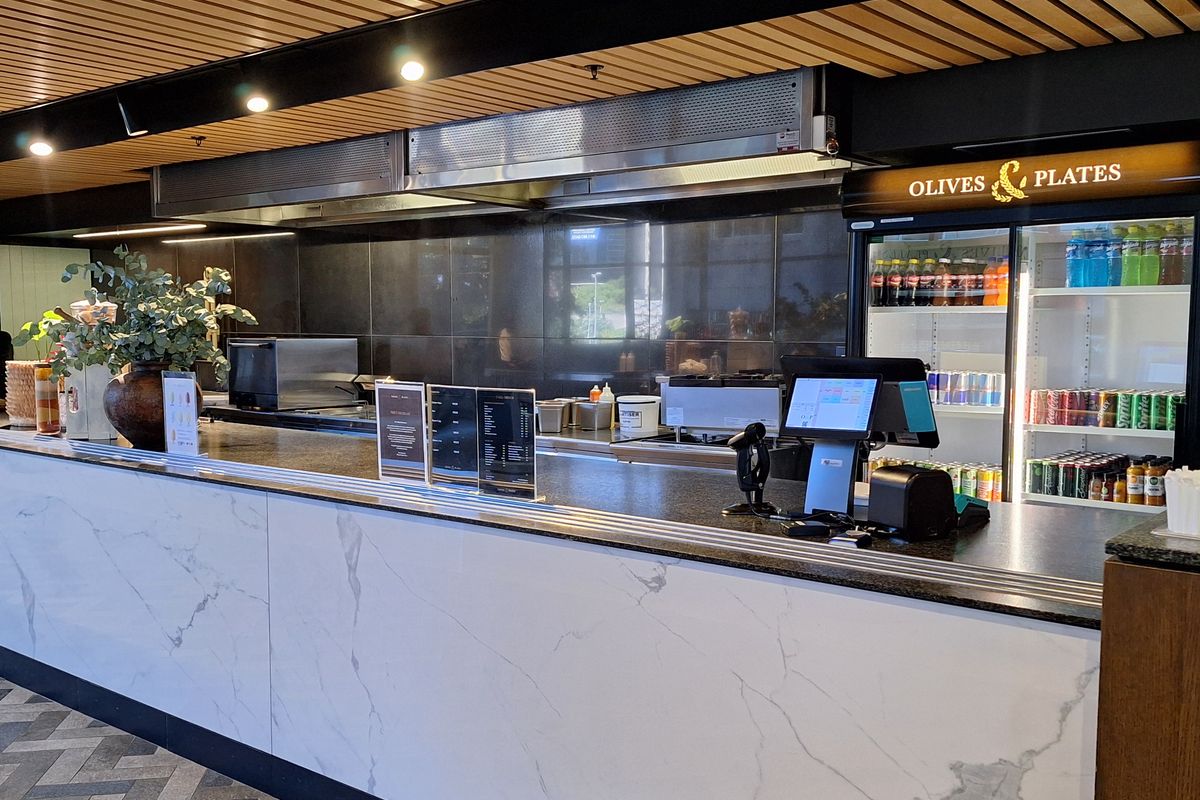 A modern commercial service counter featuring a marble-look facade, stone countertop, integrated stainless steel extractor hood, and timber slat ceiling detail.