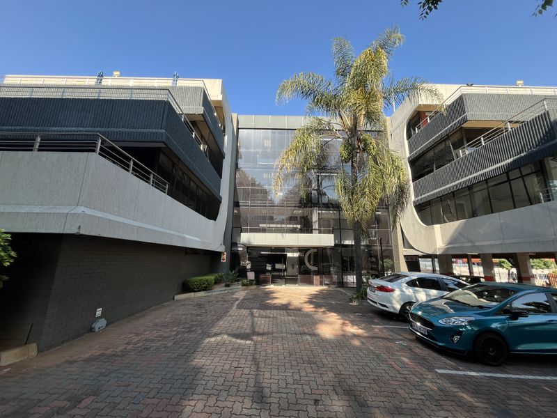 Front elevation of a multi-story office building featuring a glass facade, paved driveway, and integrated balcony structures.