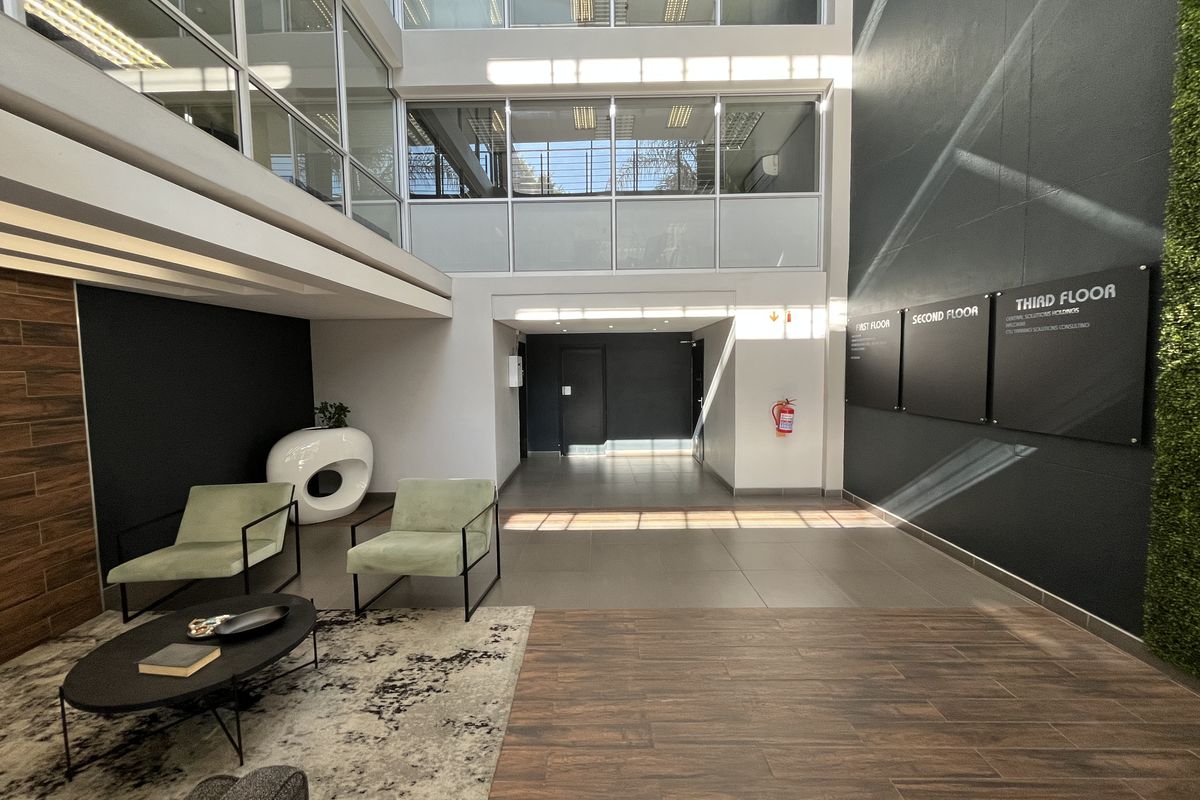 Modern office building entrance lobby featuring high ceilings, large glass windows, tiled flooring, and clear directional signage for multiple floors.