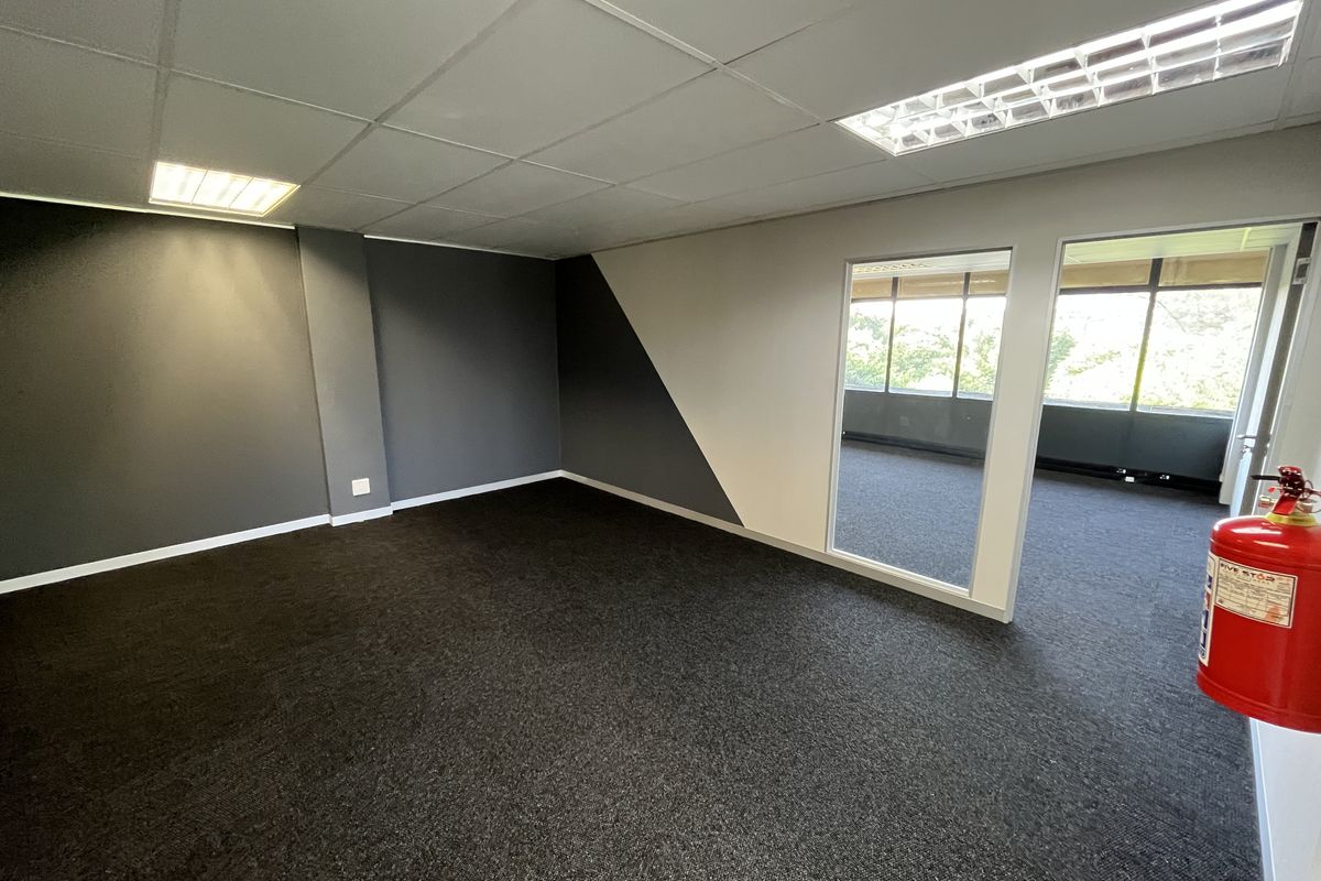 A clean, empty office space featuring dark carpet flooring, a suspended ceiling with recessed lighting, and a glass partition wall.