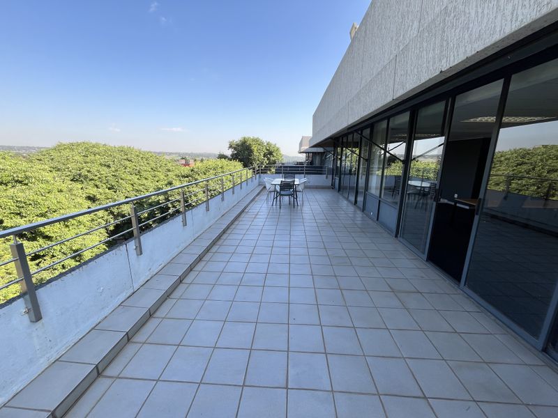 Spacious outdoor balcony featuring tiled flooring, a stainless steel balustrade, and extensive glass sliding doors providing access to the office interior.
