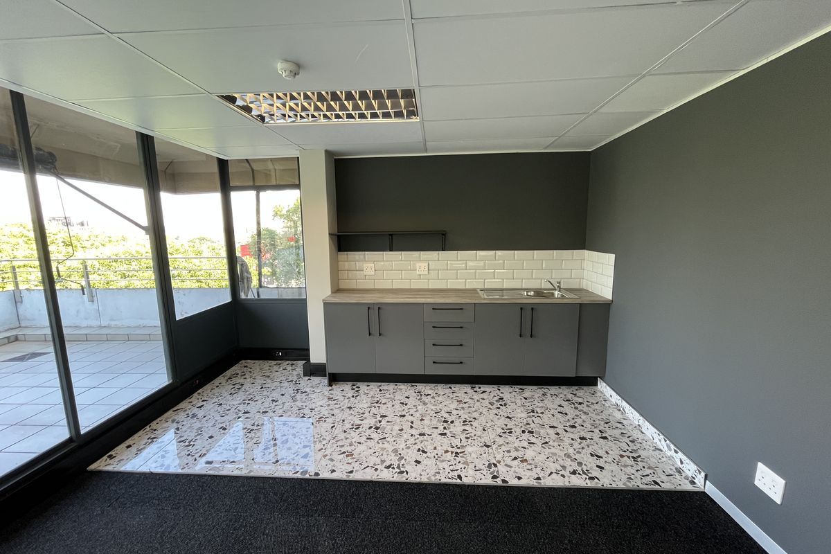 Modern office kitchenette featuring sleek grey cabinetry, subway tile backsplash, stainless steel sink, and stylish terrazzo flooring with access to a private balcony.