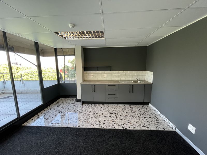 Modern office kitchenette featuring sleek grey cabinetry, subway tile backsplash, stainless steel sink, and stylish terrazzo flooring with access to a private balcony.