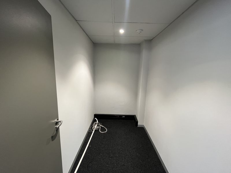 A clean, empty office space featuring neutral walls, carpeted flooring, and a suspended ceiling with integrated lighting and smoke detection.
