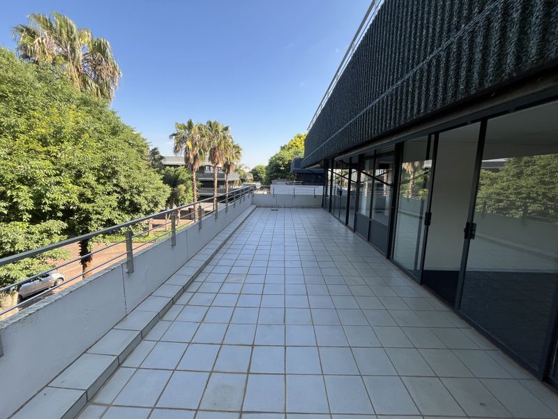 Spacious outdoor balcony featuring tiled flooring, a metal safety balustrade, and large sliding glass doors providing access to the office interior.