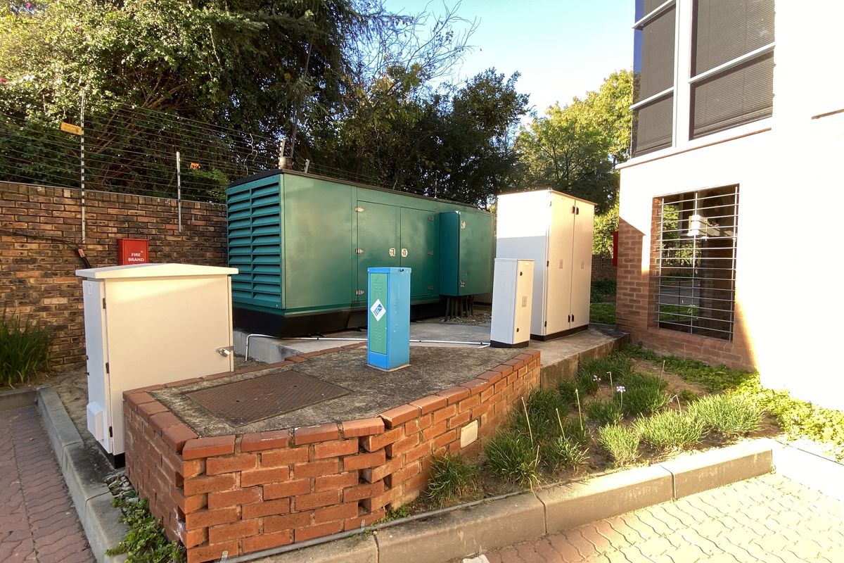 Exterior view of the office property featuring a large industrial backup generator, electrical distribution cabinets, and brick retaining wall infrastructure.