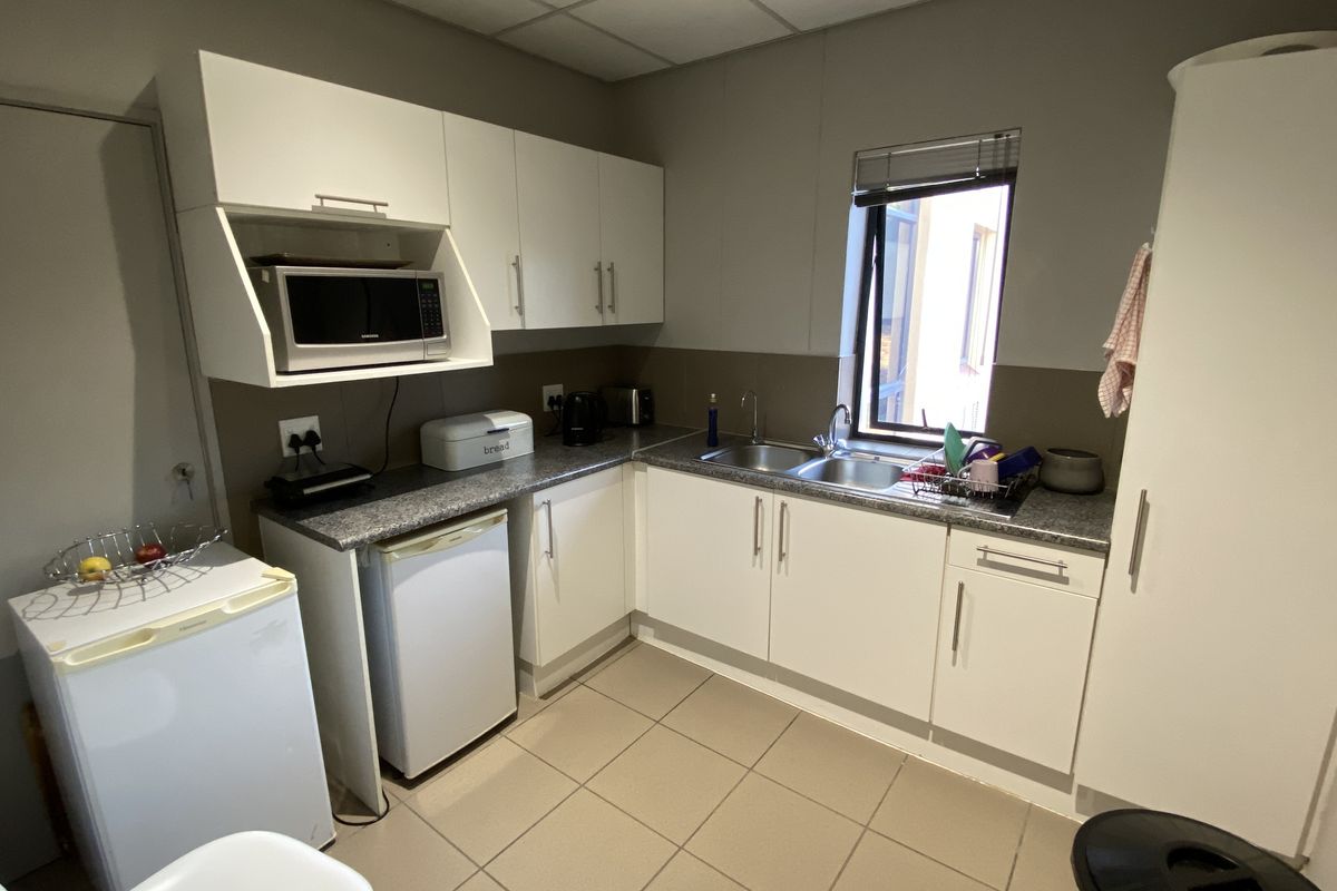 A compact office kitchenette featuring white cabinetry, granite-look countertops, a stainless steel double sink, and tiled flooring.