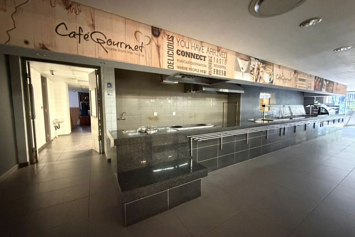 A commercial kitchen or cafe service area featuring a long granite countertop, built-in cooking station, and tiled flooring in an office environment.