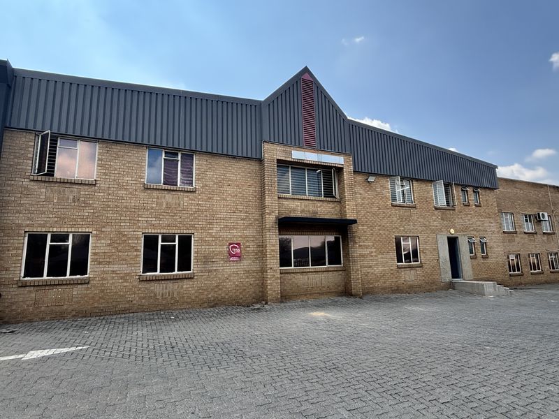 A well-maintained industrial building featuring a face brick facade, metal roofing, and a paved exterior parking area.