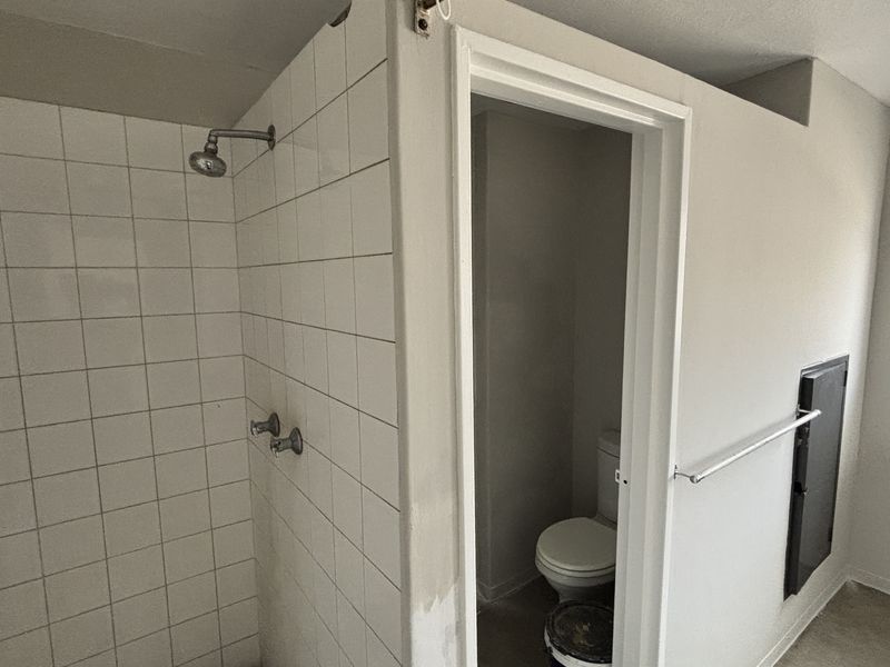 A functional bathroom featuring a tiled shower enclosure, separate toilet area, and wall-mounted basin, requiring cosmetic updates to improve its overall condition.