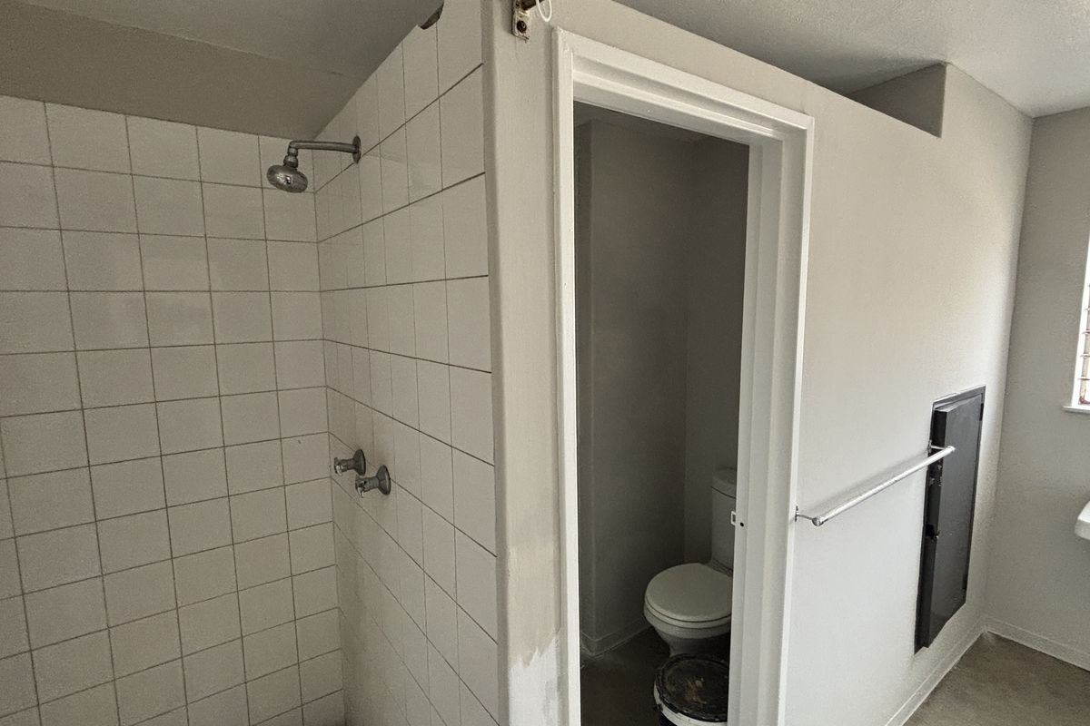 A functional bathroom featuring a tiled shower enclosure, separate toilet area, and wall-mounted basin, requiring cosmetic updates to improve its overall condition.