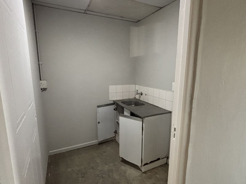 A small utility or scullery area featuring a stainless steel sink, tiled splashback, and basic built-in cabinetry in need of maintenance.