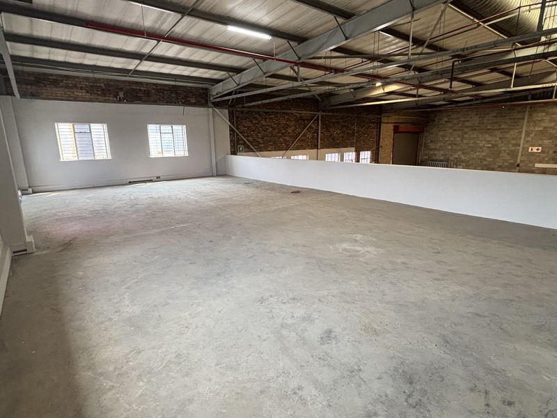 Spacious open-plan industrial mezzanine area featuring exposed steel trusses, brickwork walls, concrete flooring, and functional overhead lighting.