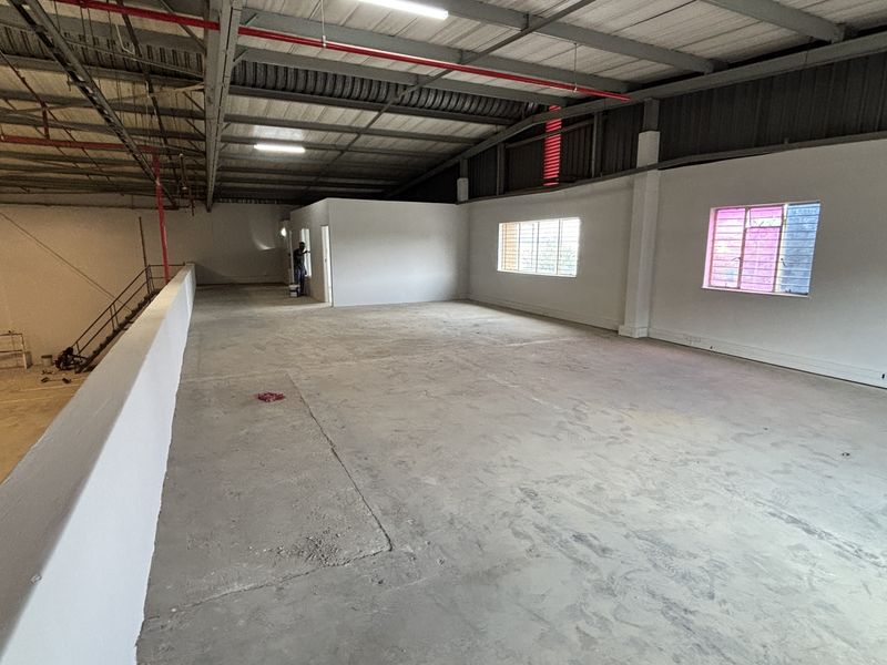 Spacious industrial mezzanine area featuring exposed steel roof trusses, fire sprinkler system, and concrete flooring, suitable for storage or office conversion.